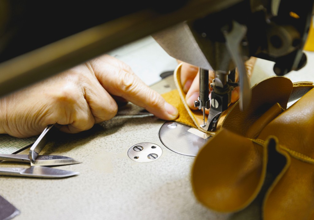 職人の手がミシンで革を丁寧に縫い合わせている様子が写っており、手作業による細やかな技術が伝わる