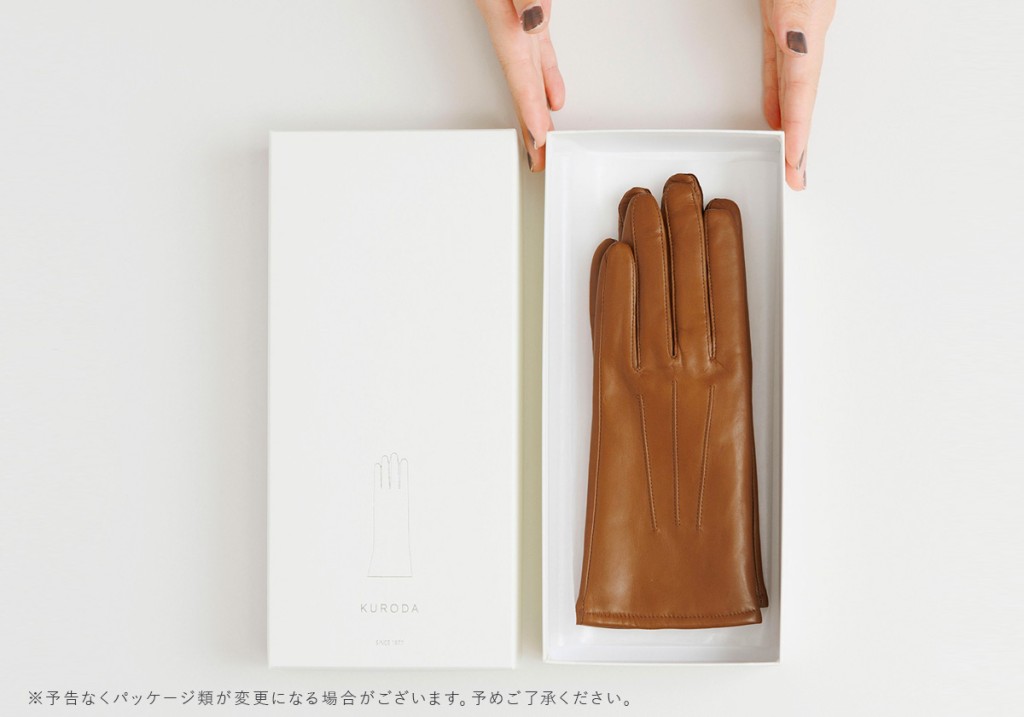 白い箱に丁寧に収められた茶色のKURODAクロダの革手袋を、女性の手が上品に開封している様子を写した写真